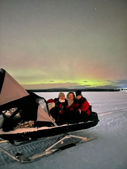 A group of people in a sled on a snowy landscape under a night sky with aurora borealis. 2
