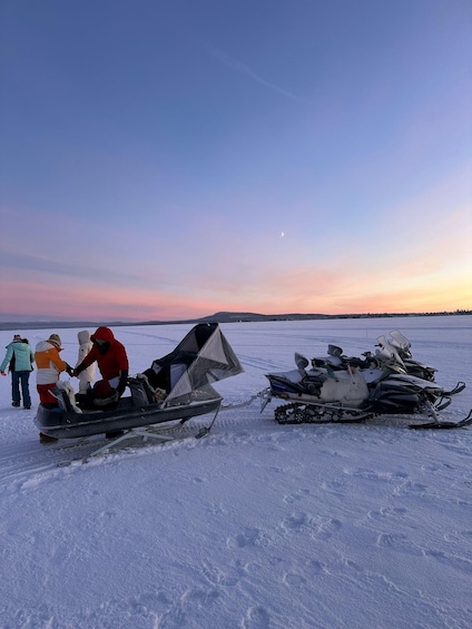 A snowy landscape with two snowmobiles and people in winter clothing. 1