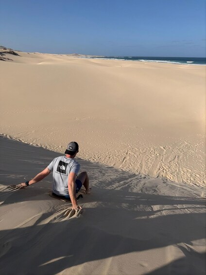 A person sitting on a sand dune with a beach and ocean in the background. 4