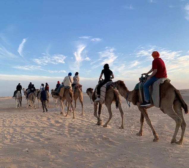 A group of people riding camels across a desert landscape. 1