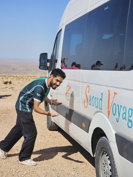 A man in a green shirt and black pants approaching a white van with 'Saoud Voyage' written on it. 5