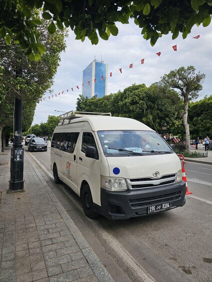 A white van parked on a city street with trees and a tall building in the background. 5