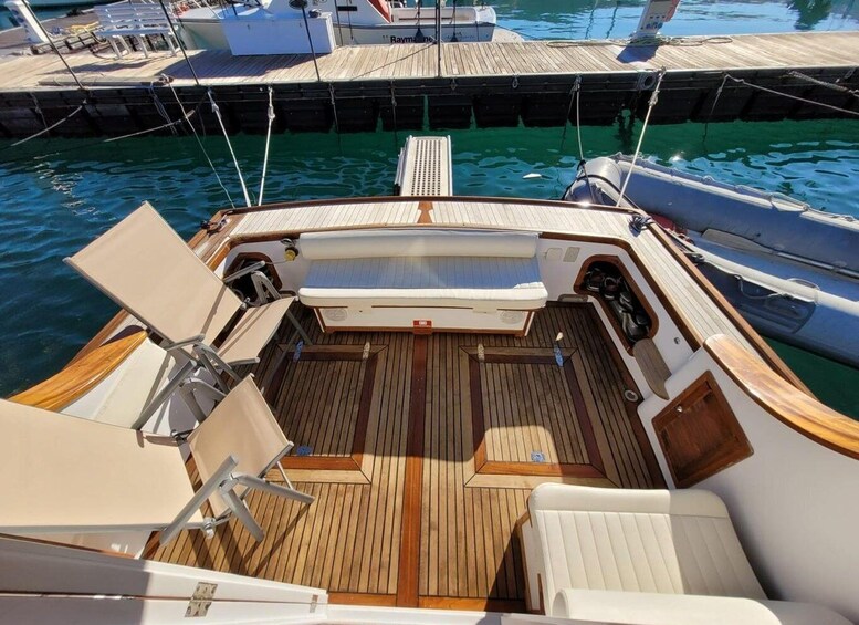 A boat's deck with wooden flooring, white cushioned seats, and a central table. 3