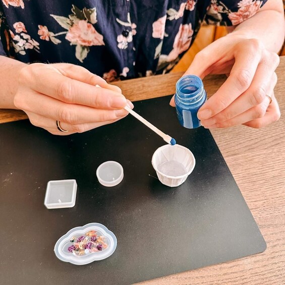 A person pouring blue liquid from a bottle into a small white container. 3