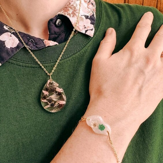 A person wearing a green sweater with a floral scarf, a gold necklace, and a bracelet with a green flower. 5