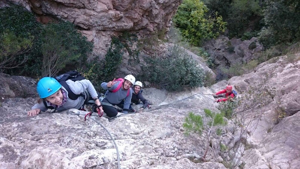 Three people rappelling down a rocky cliff with vegetation around. 4
