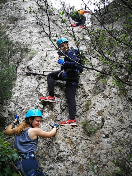 Two people rock climbing a rocky cliff with safety harnesses and helmets. 2