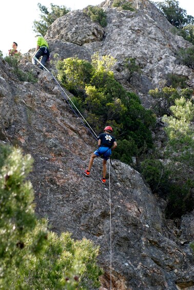 A person rappelling down a rocky cliff with vegetation around. 3