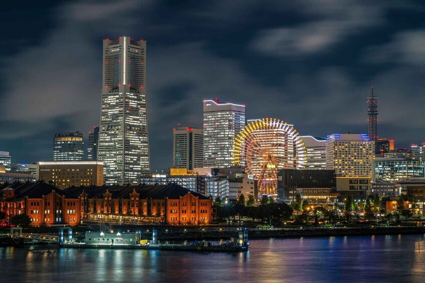 A city skyline at night with illuminated skyscrapers, a large Ferris wheel, and a river reflecting the lights. 1