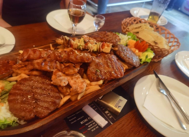 A variety of grilled meats and vegetables on a wooden serving board, accompanied by bread and a basket of fries. 3