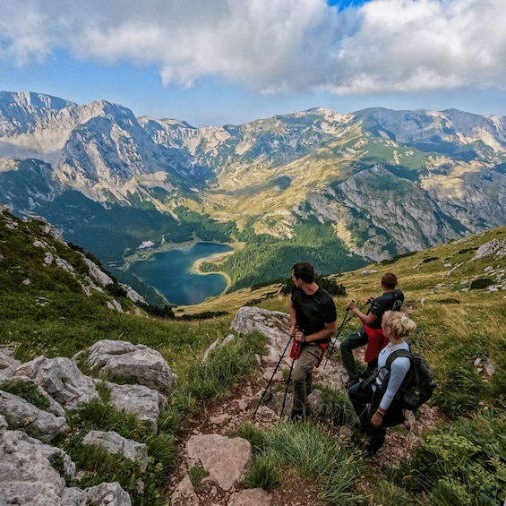 Hikers on a mountain trail with a lake and mountains in the background. 2