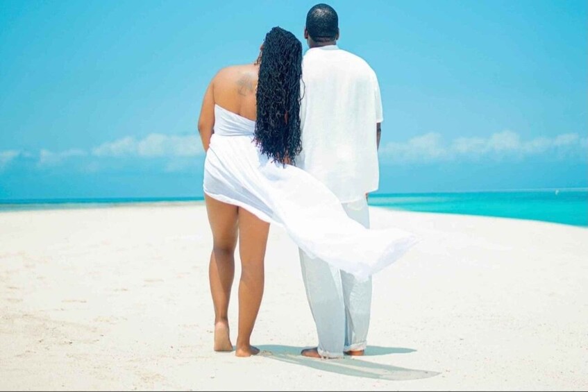 A couple standing on a beach with a clear sky and ocean in the background. 3