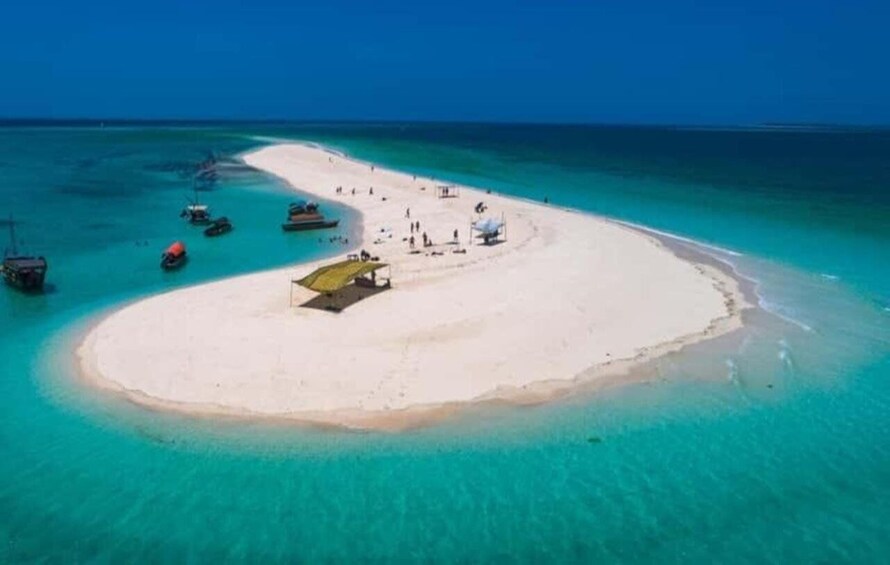 A small island with clear turquoise waters, a sandy beach, and several boats anchored nearby. 5