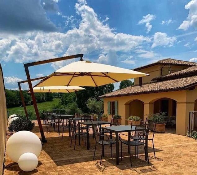 An outdoor patio with tables and chairs, a pergola with a yellow umbrella, and a building with a tiled roof. 5