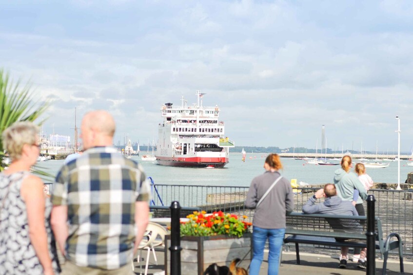 A ferry docked at a harbor with people walking by and a bench in the foreground. 2