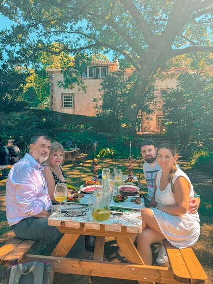 A group of people dining outdoors at a wooden table with food and drinks. 4