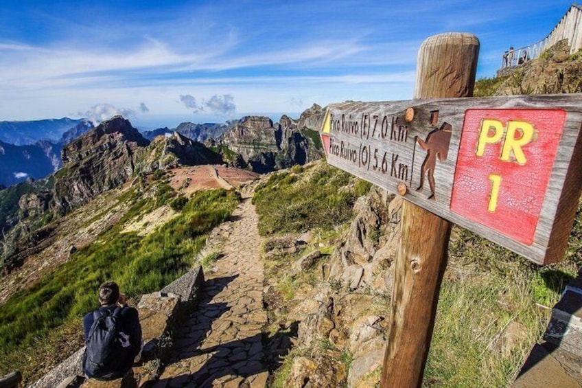 Un cartel de sendero con indicaciones de altitud y una persona sentada en el camino. 5