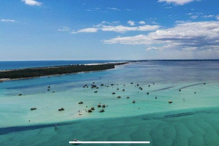 A coastal area with clear turquoise waters, a sandy beach, and a breakwater. 3