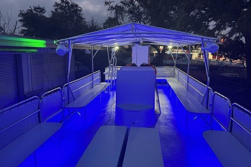 A boat with blue lighting, metal railings, and benches. 4