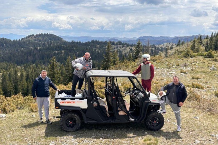 Vier Personen stehen neben einem Golfwagen auf einer Wiese, im Hintergrund sind Berge zu sehen. 3