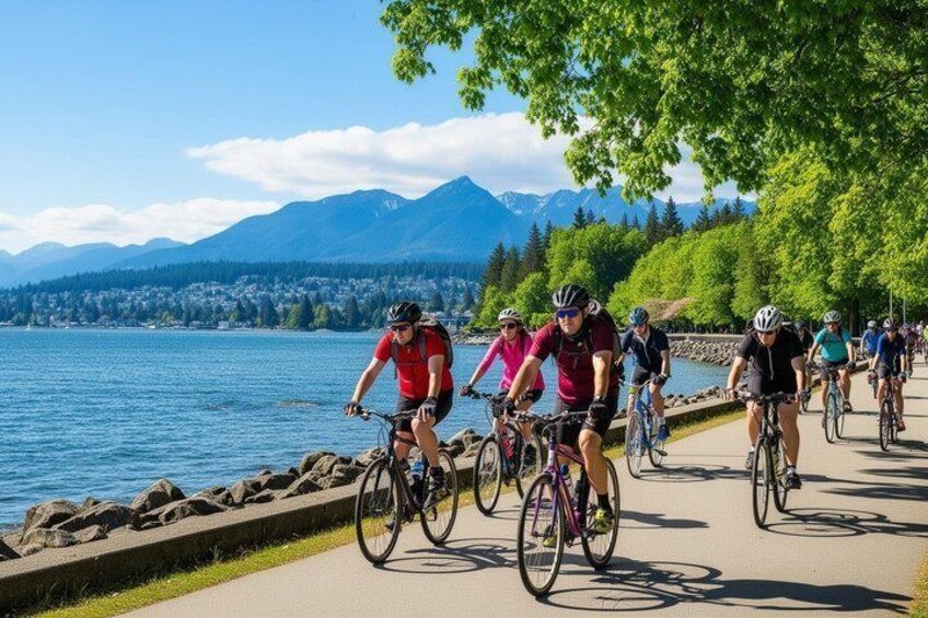Cyclists on a paved path by a lake with mountains in the background. 3
