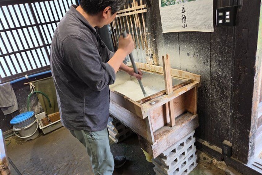 A person working with wooden tools in a workshop with a wooden table and a sign with Japanese characters. 2