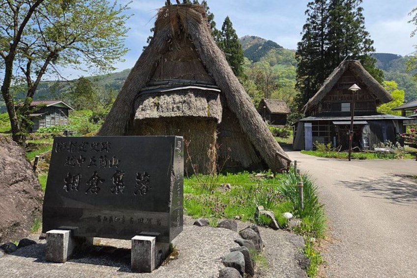A traditional thatched-roof house, a sign with Japanese characters, and a modern building in a rural setting. 3