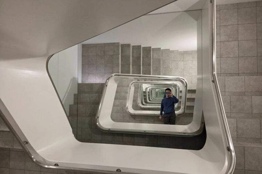 Una estructura arquitectónica moderna con una escalera de paredes de cristal y una persona de pie en el nivel superior. 1