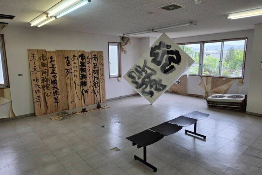 Una habitación con esteras de tatami, un banco negro y un gran pergamino colgado con caligrafía. 5