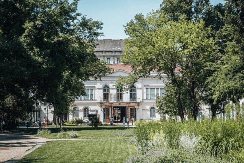Un edificio histórico con jardín delantero, rodeado de árboles. 4
