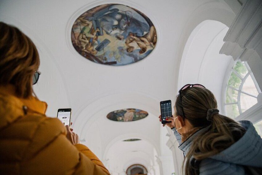 Two people inside a building with arched ceilings and circular paintings. 3