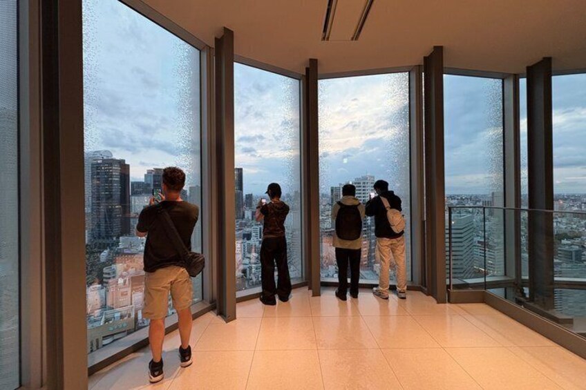 A group of people standing in a high-rise building with large windows overlooking a cityscape. 5