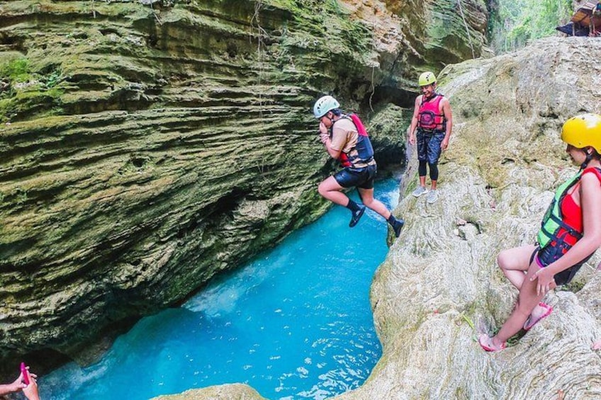 People engaging in a water activity, possibly jumping or rappelling, in a rocky canyon with a blue water body. 2