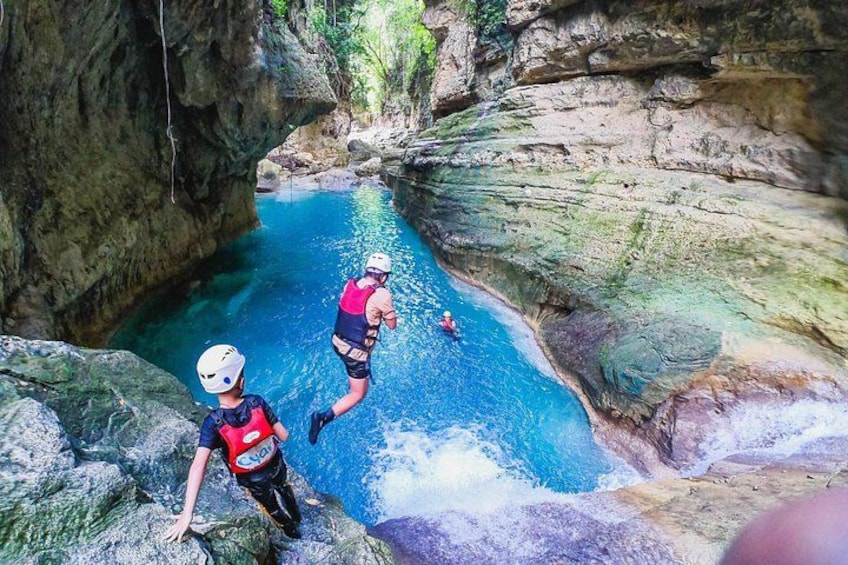 Two people rappelling into a clear blue water body surrounded by rocky cliffs. 3