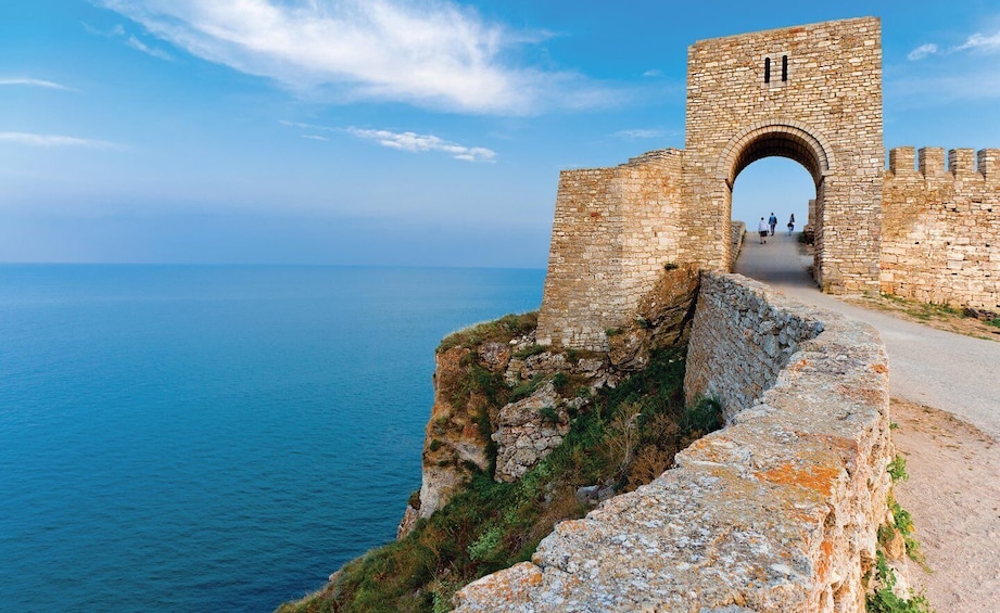 A stone archway leading to a coastal path with a clear view of the sea. 2
