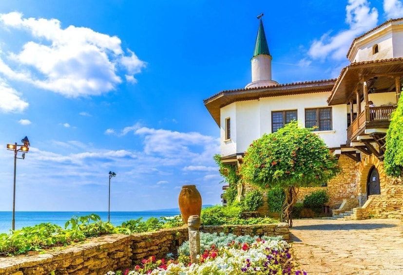 A coastal building with a green spire, stone walls, and a garden with colorful flowers. 3