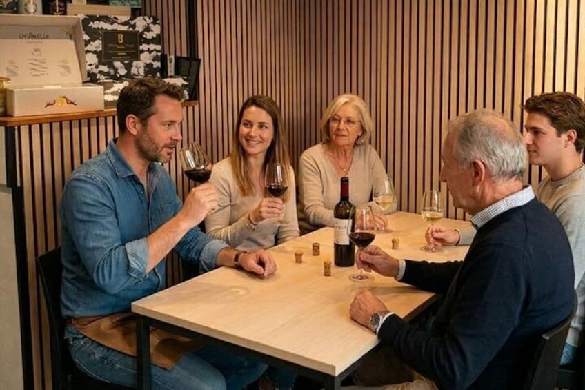 A group of people sitting around a table with wine glasses, in a room with vertical wooden slats on the walls. 4