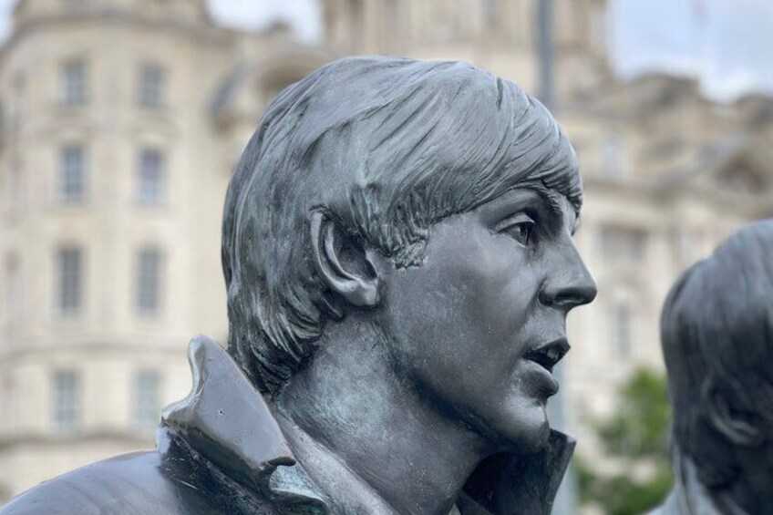 En statue af en mand med uskarpt ansigt, iført en jakke, og en bygning i baggrunden. 1