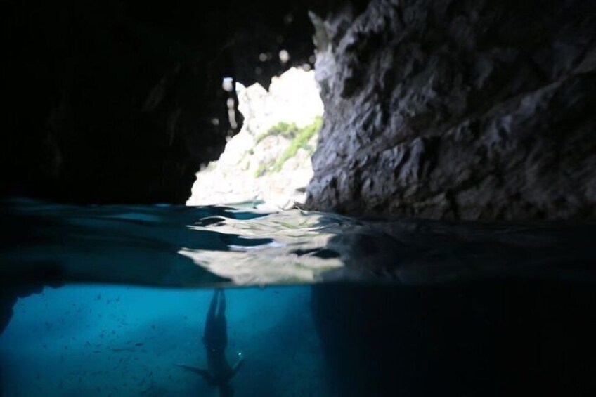 En dykare under vatten i en grotta med en bergig vägg och en klar, blå pool. 2