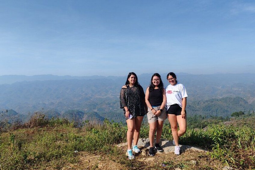 Three people standing on a hill with a mountainous landscape in the background. 2