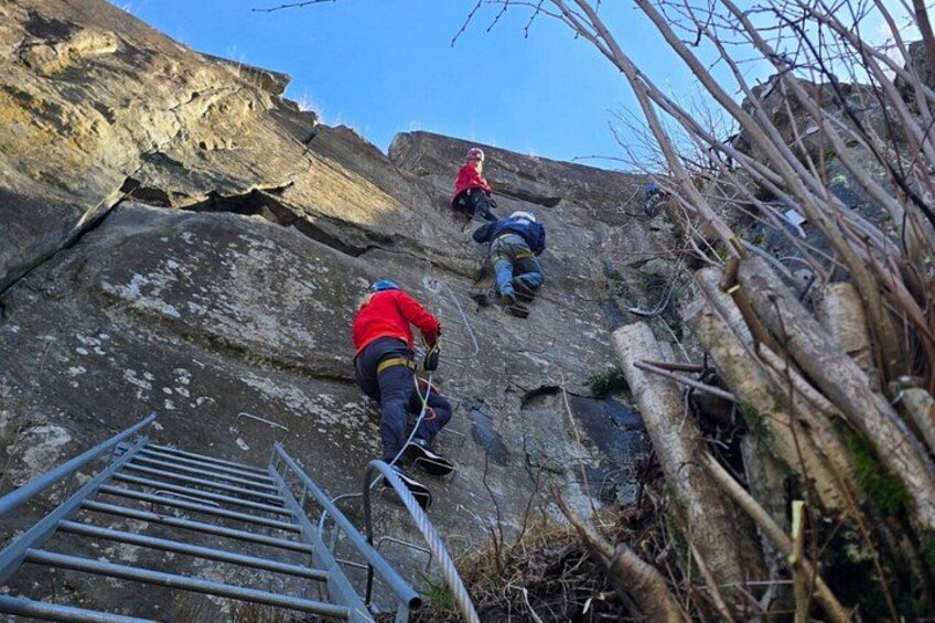 Three people climbing a rocky mountain with a metal ladder. 5