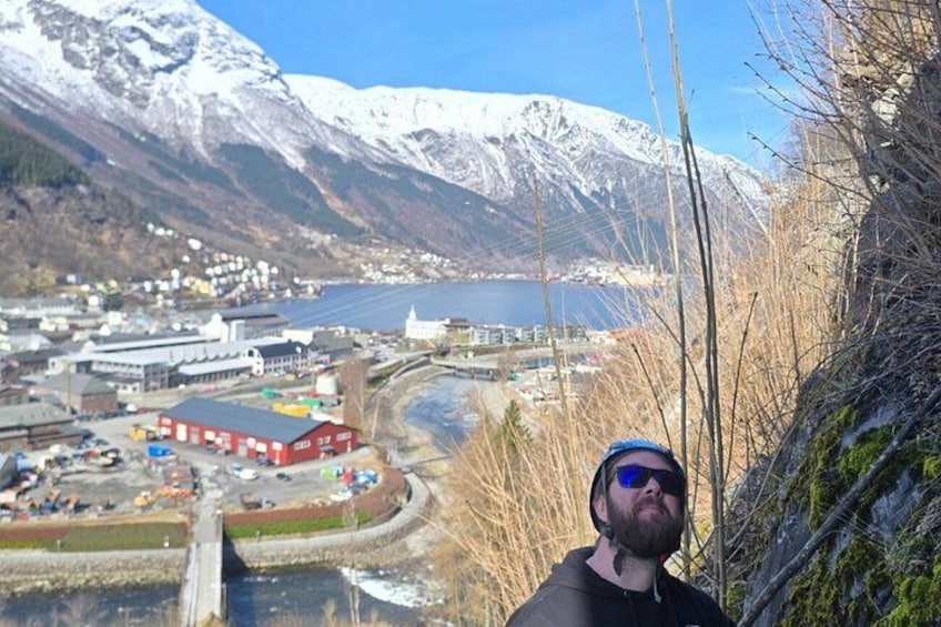 A mountainous landscape with a river, buildings, and a person standing on a bridge. 1