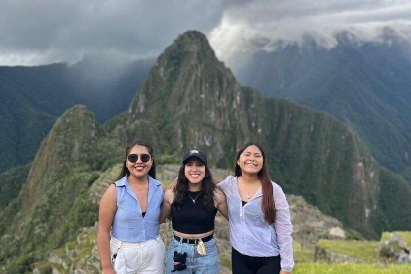 Three individuals standing in front of Machu Picchu with a mountainous landscape in the background. 1