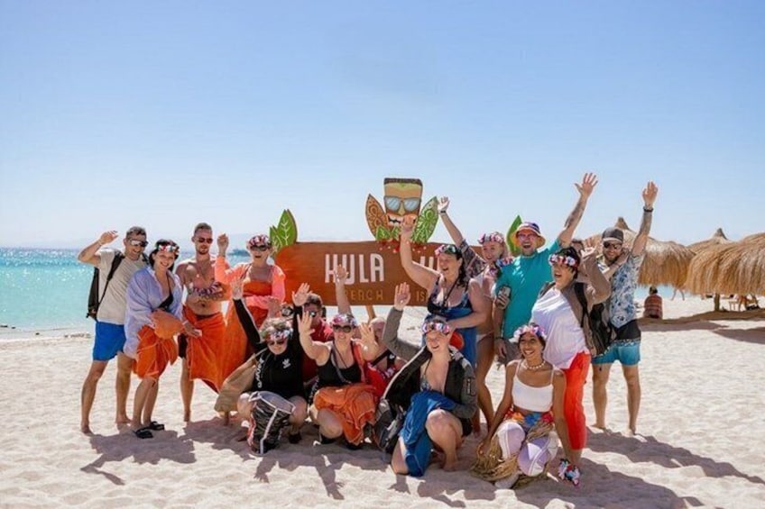 Un groupe de personnes sur une plage, à côté d’un panneau sur lequel on peut lire : « HULA ENCH. » 1