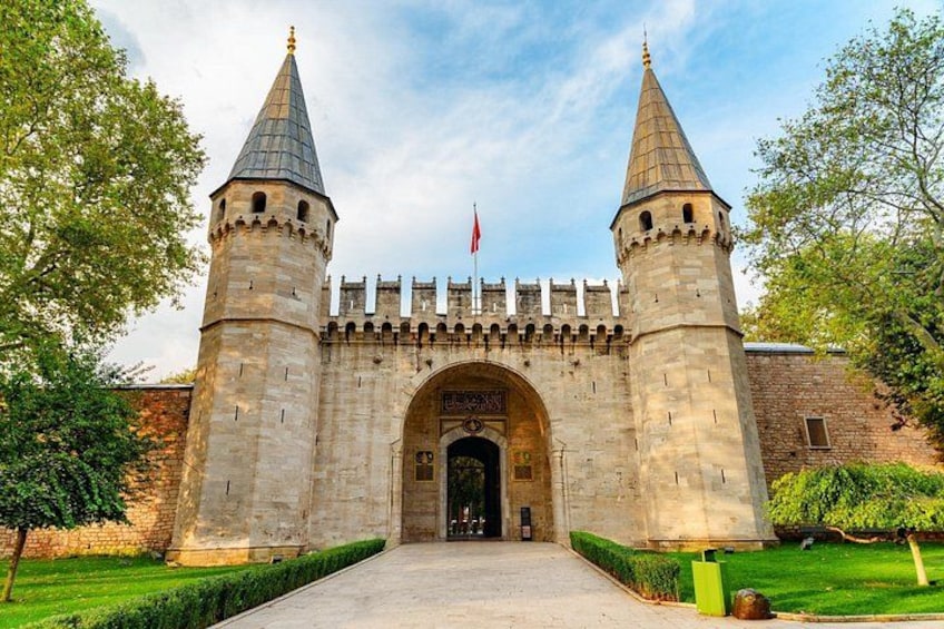 A historic stone gatehouse with two towers, a flag, and a well-maintained lawn. 3