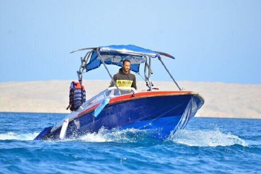 Een blauwe en rode boot met een zonnedak, die door helderblauw water vaart. 1