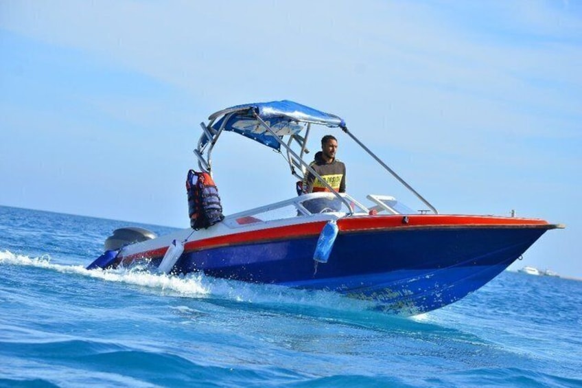 Een blauw-rode speedboot met een zonnedak, een persoon met een reddingsvest en een andere persoon in een gele shirt op het dek. 5