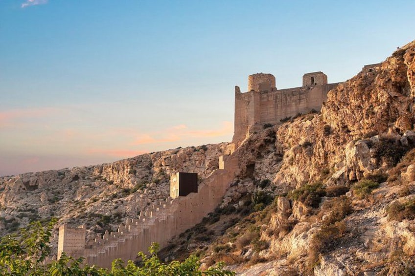 Eine historische Steinmauer mit Türmen, unwegsames Gelände und spärlicher Vegetation. 1
