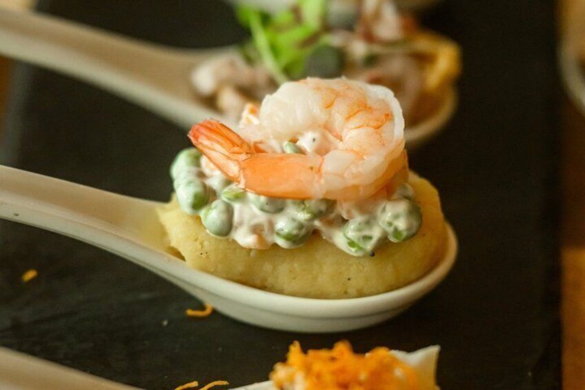 Une cuillère contenant des crevettes, des petits pois et une garniture crémeuse, le tout posé sur une base ronde. 3
