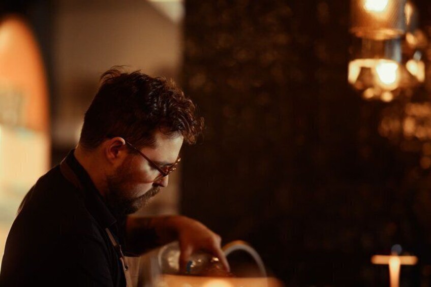 Une personne qui travaille derrière un comptoir de bar, peut-être un barman, avec un arrière-plan flou qui suggère un lieu intérieur. 2